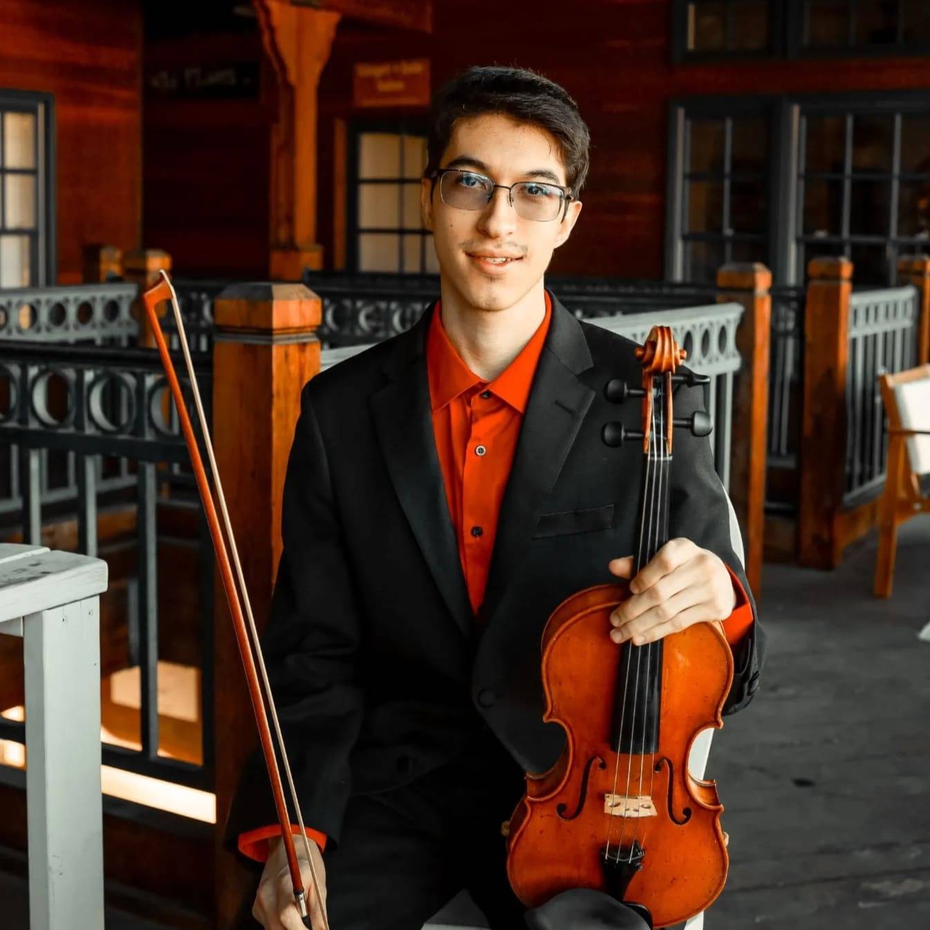 Marcus with his acoustic violin, wearing a black suit and red shirt
